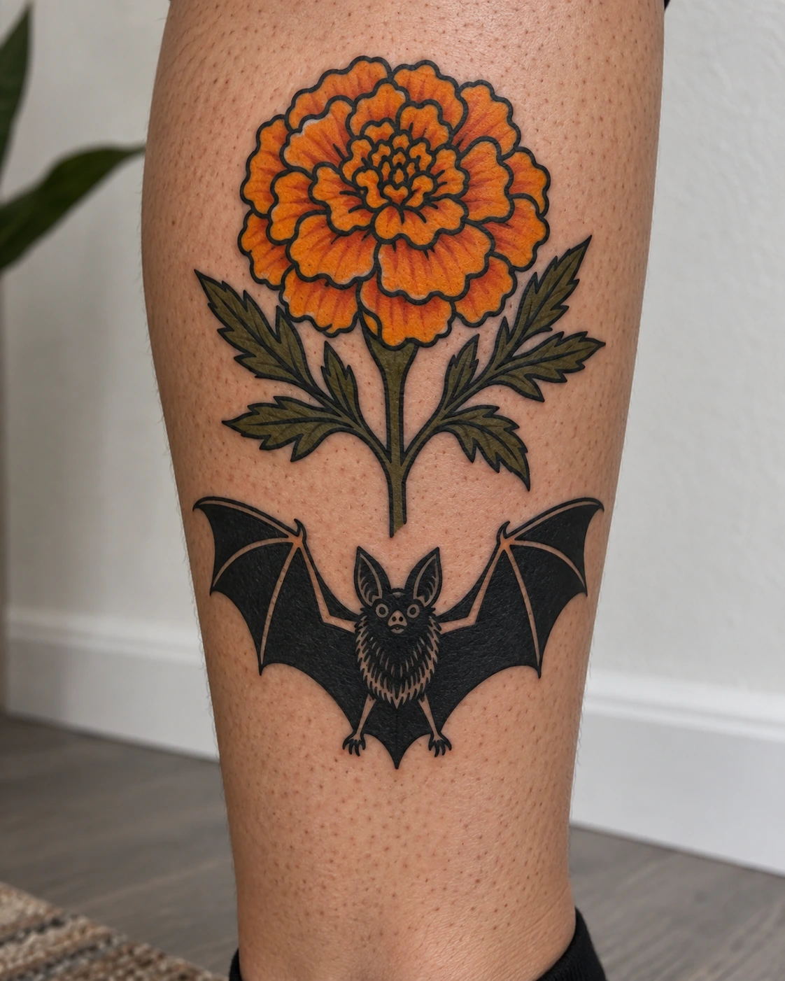 Black bat and orange marigold tattoo on the calf