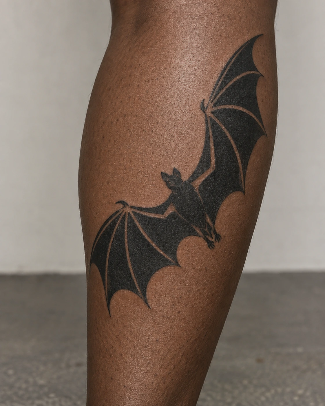 Bold blackwork bat tattoo with open skin channels on the calf