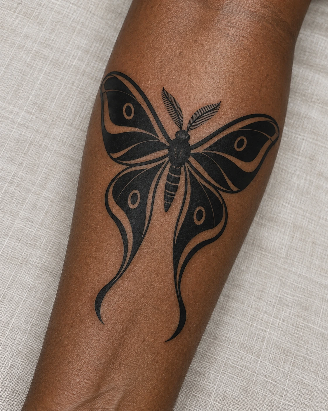 Bold blackwork luna moth tattoo with open skin patterns and curved hindwing tails on the forearm