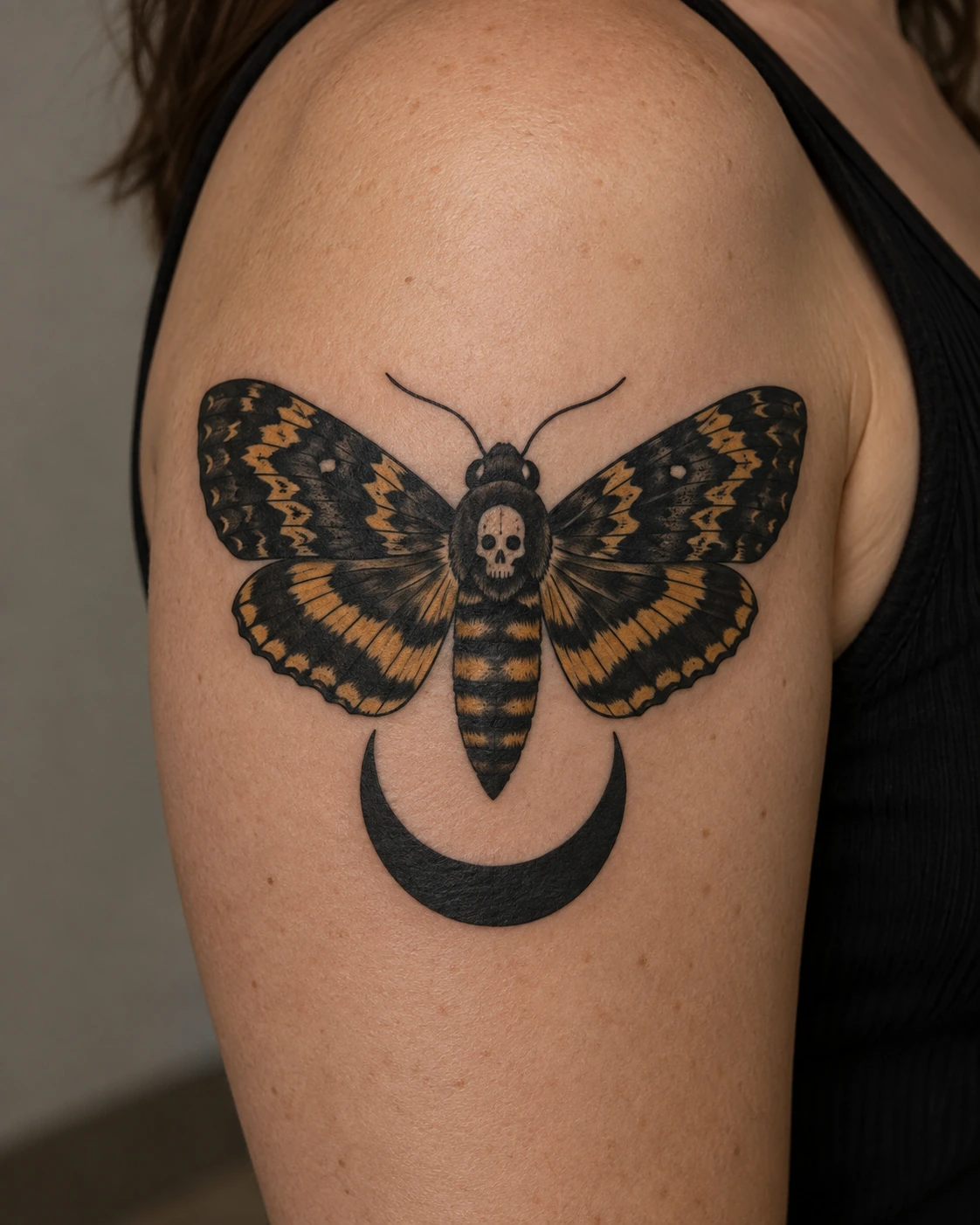 Black and gold death's-head moth tattoo concept above a crescent on the upper arm