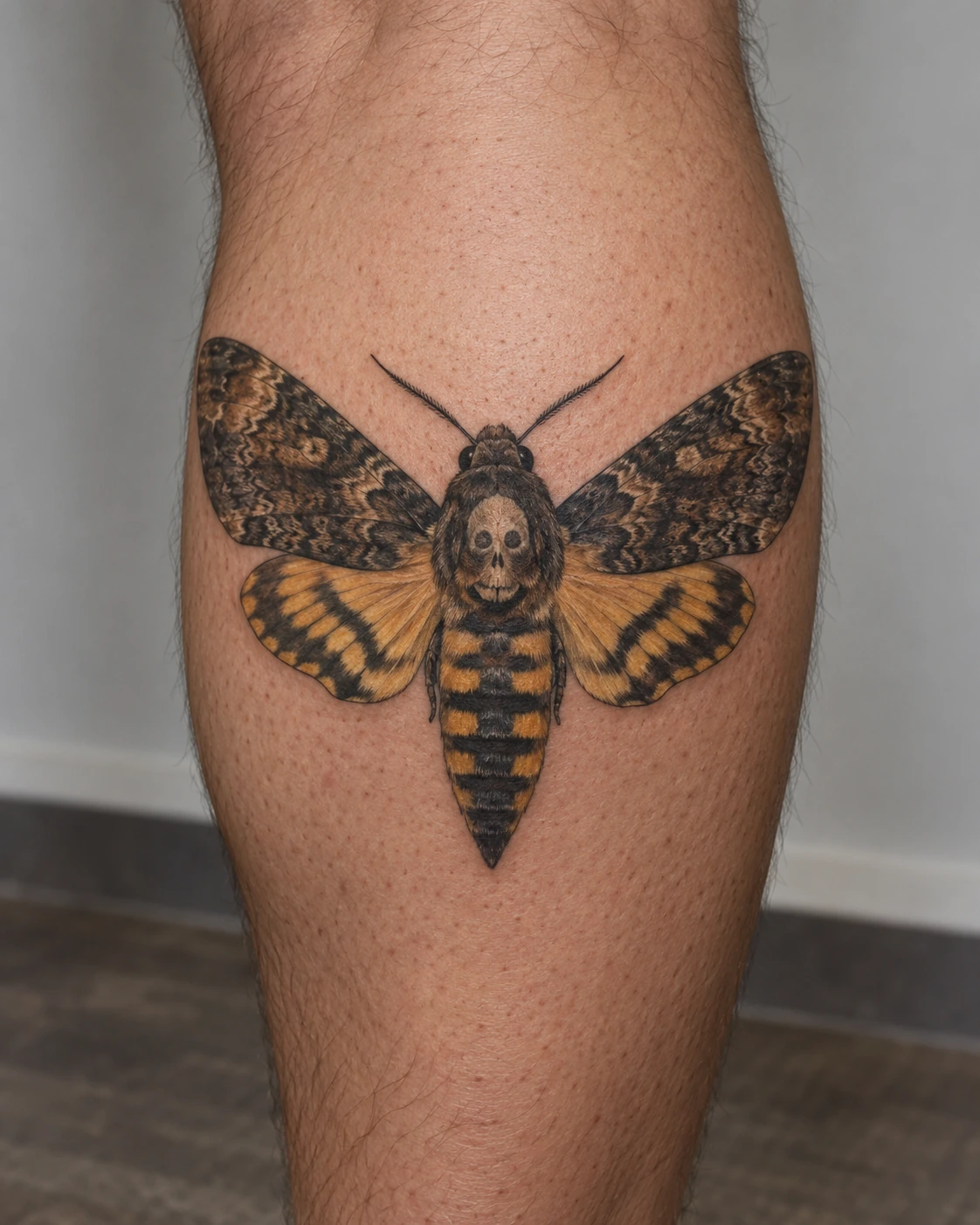 Brown and ochre death moth tattoo with a skull motif on the calf