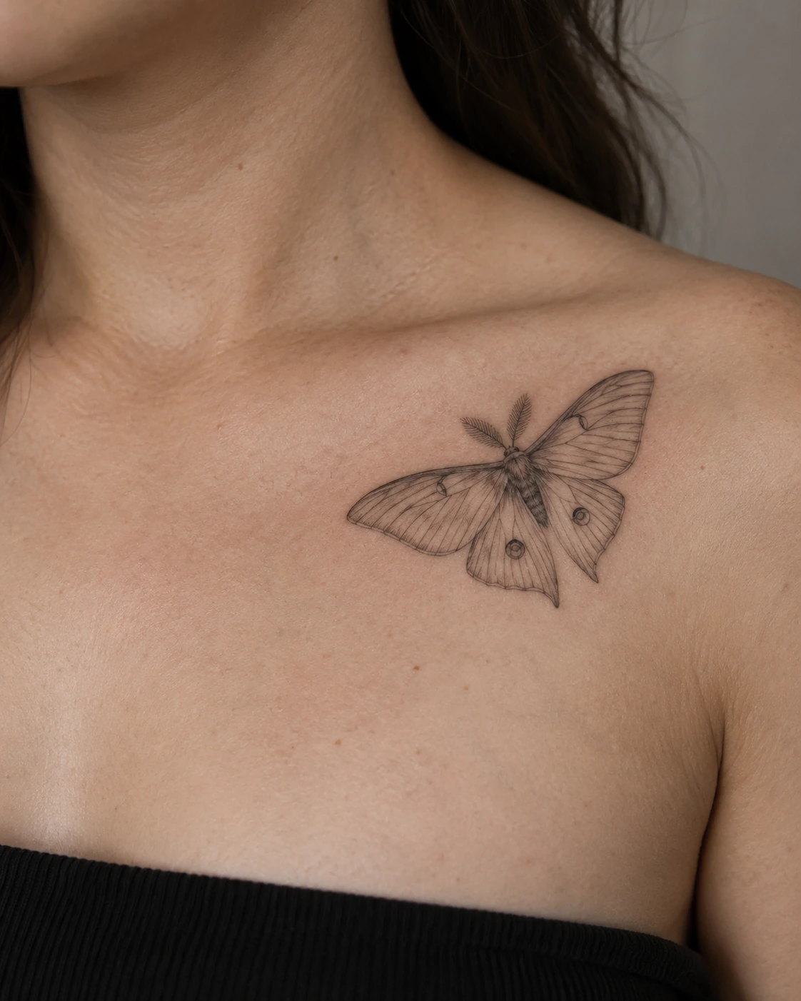 Fine-line moth tattoo concept placed diagonally below the collarbone