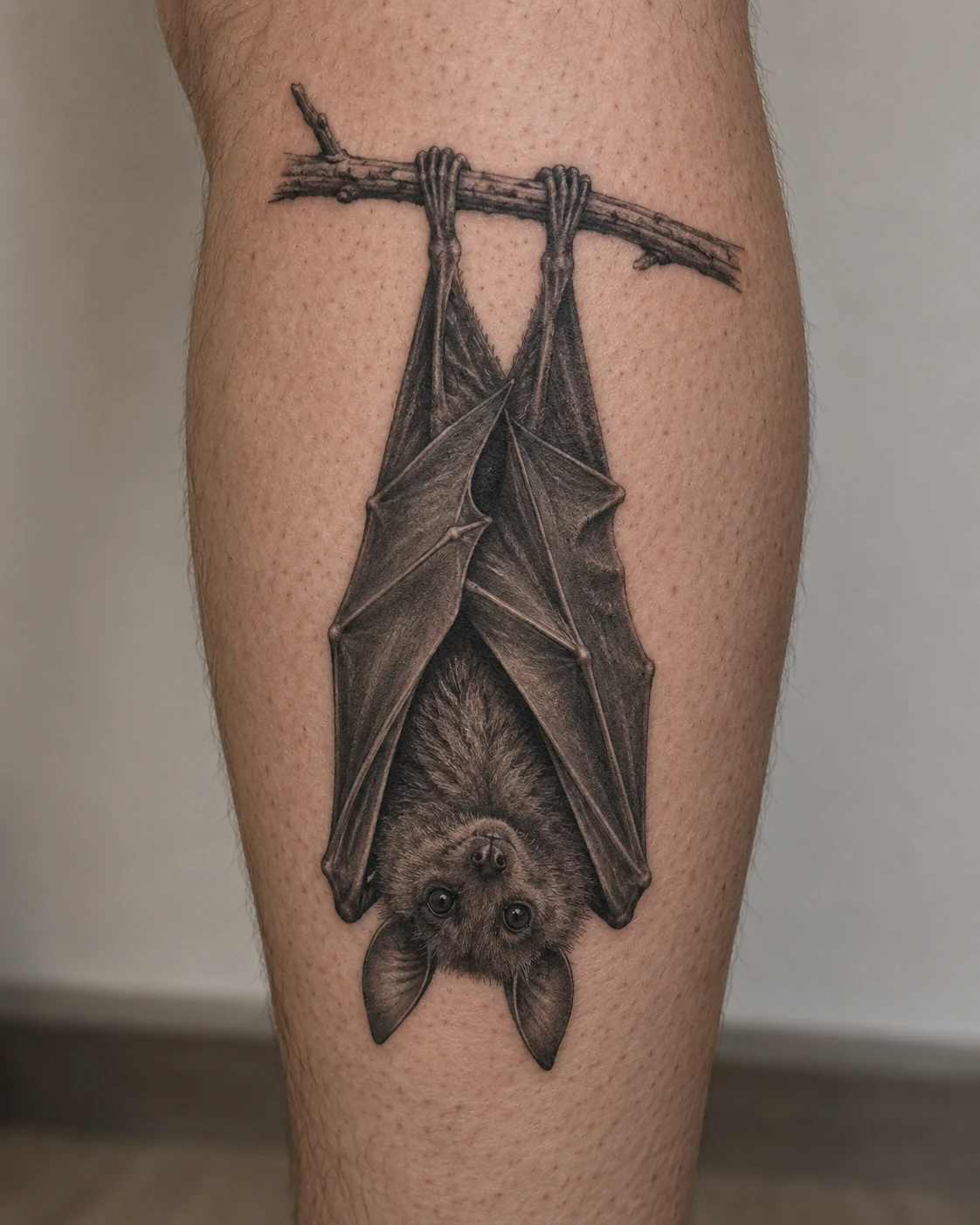 Upside-down bat tattoo hanging from a short branch on the calf