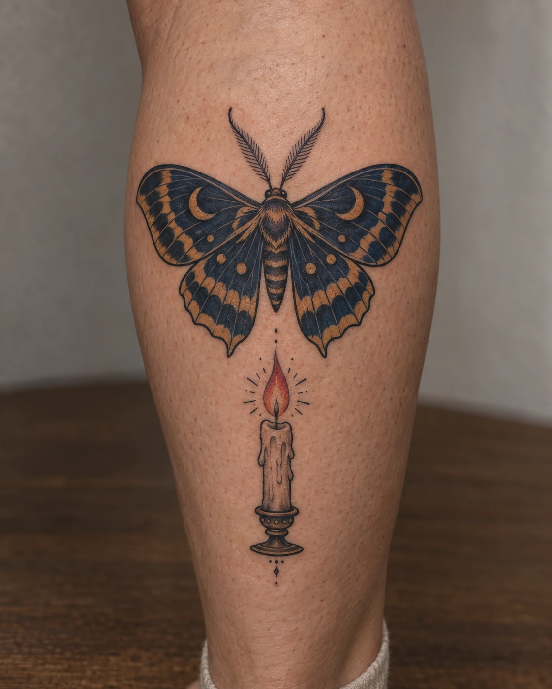 Traditional blue and ochre moth tattoo concept above a candle on the calf