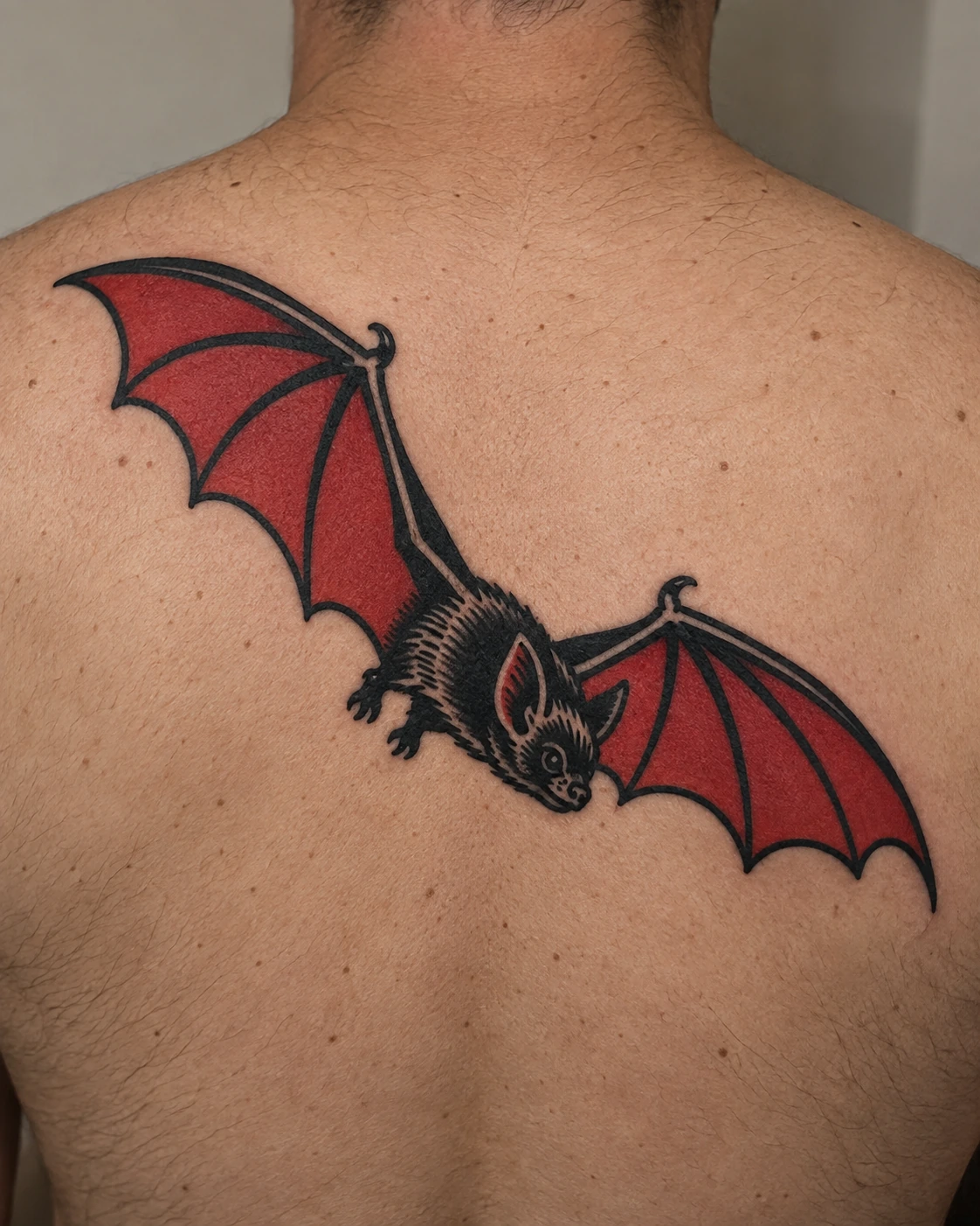 Red and black diving bat tattoo on the upper back