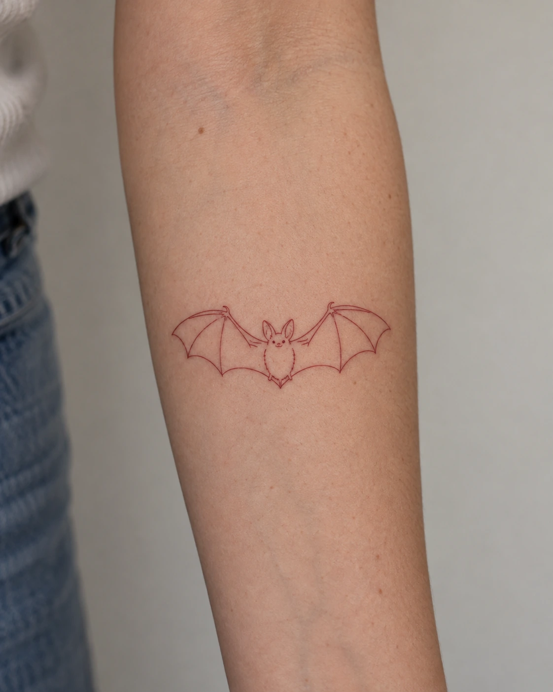 Fine dark-red bat outline tattoo on the forearm