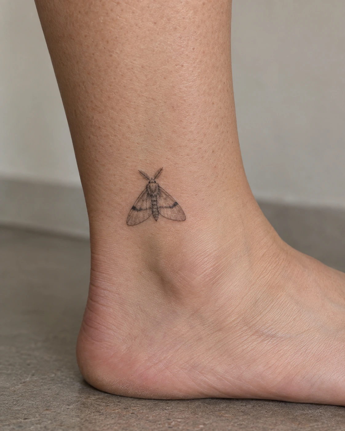 Simple folded-wing moth tattoo concept above the ankle
