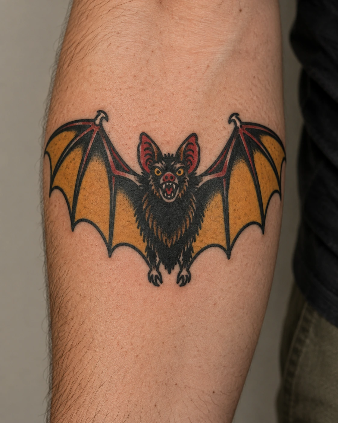 Traditional bat tattoo in mustard, black, and red on the forearm